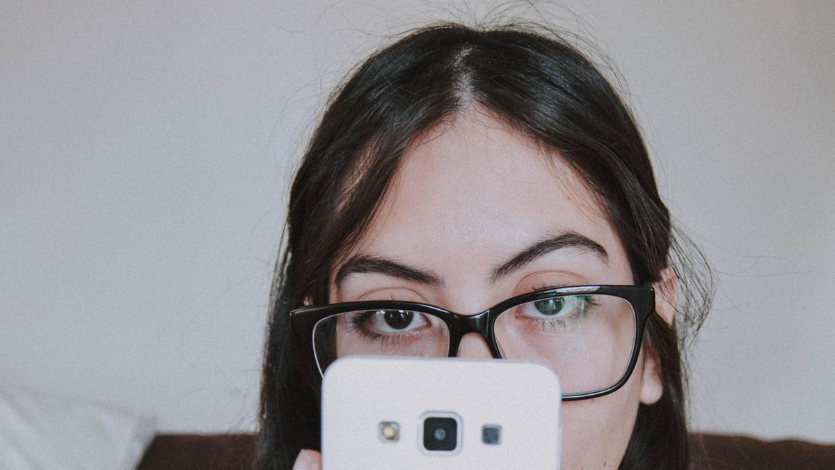 Una joven con gafas mira la pantalla de su móvil.