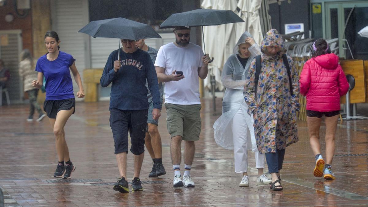 Un grupo de personas practica deporte y pasea por Las Canteras bajo la lluvia este sábado.