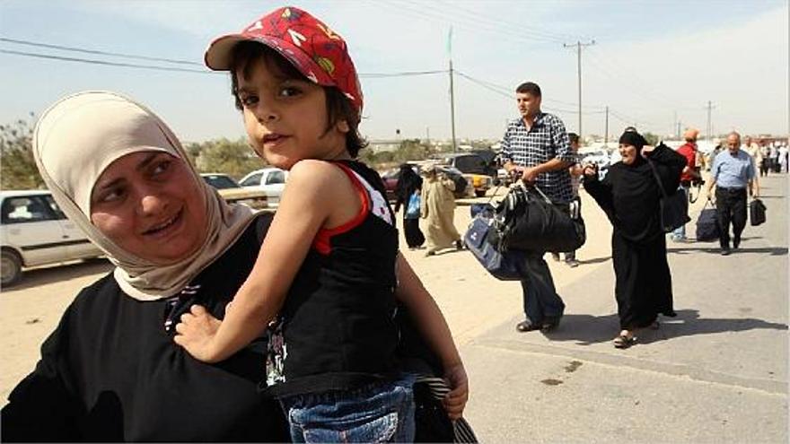 Una mujer cruza con su hija en brazos  la reabierta frontera de Gaza con Egipto junto a cientos de palestinos.