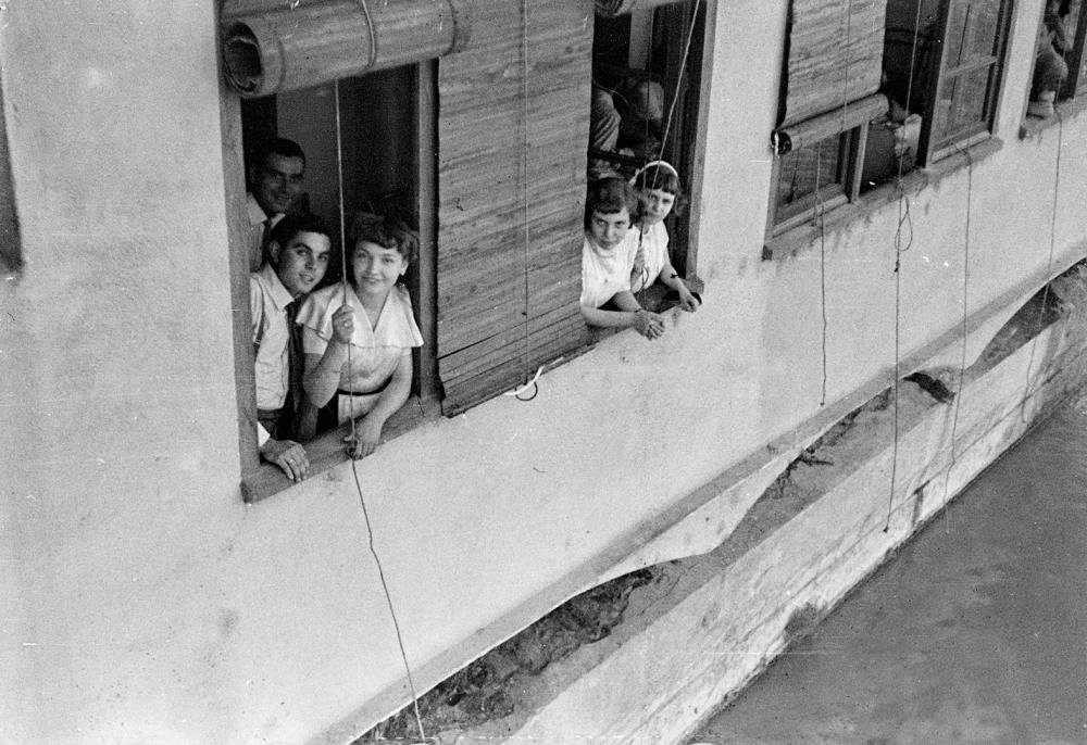 Un grup de joves somriuen a la càmera del fotògraf des de la finestra d'un habitatge amb vistes al riu Onyar. Es tracta d'un retrat de grup en un indret reconeixible de la ciutat. Malgrat l'aparent quotidianitat d'aquesta escena, el fotògraf transmet amb aquesta imatge una visió molt personal del què està succeint davant de la seva càmera. L'inusual punt de vista, l'enquadrament que s'ha triat i la composició de l'escena es posen al servei de la creativitat i per interpel·lar directament a l'experiència del futur observador.
