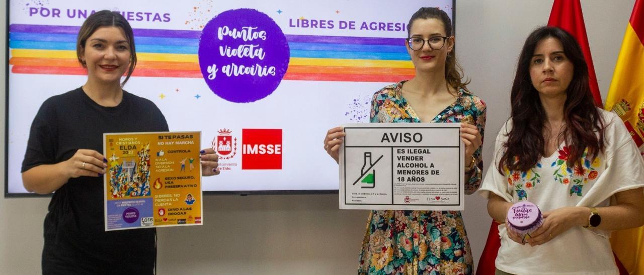 Las concejalas Anabel García y Sarah López con los carteles de la campaña y la edil Alba García mostrando el cubre vaso.