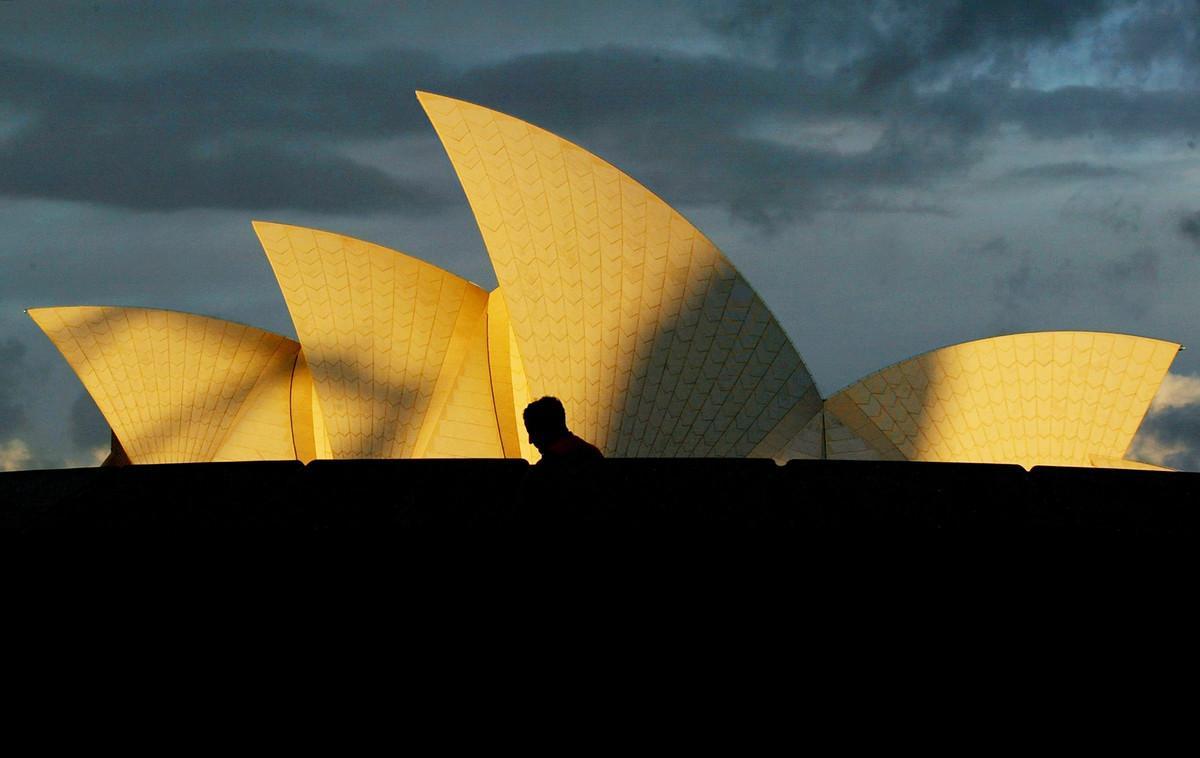 A tourist walks past the Sydney Opera House as a storm approaches overhead at sunset May 30, 2002. Australia’s top tourism attraction will receive a $A69 million (US$31 million) make-over during the next six years which will follow designs by the original Danish architect Joern Utzon. The improvements will include the construction of grand columns on the ground level, the orchestra pit will be extended and the seating refurbished, which will mean it will be closed for a year from late 2004.      REUTERS/David Gray