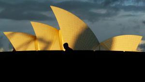 A tourist walks past the Sydney Opera House as a storm approaches overhead at sunset May 30, 2002. Australia’s top tourism attraction will receive a $A69 million (US$31 million) make-over during the next six years which will follow designs by the original Danish architect Joern Utzon. The improvements will include the construction of grand columns on the ground level, the orchestra pit will be extended and the seating refurbished, which will mean it will be closed for a year from late 2004.      REUTERS/David Gray