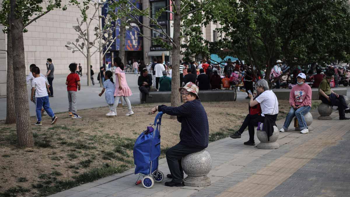 Personas mayores descansan en una calle de Beijing, junto a niños que juegan