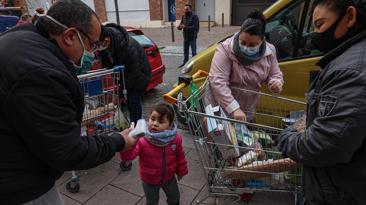 Una niña espera mientras su madre rellena la bolsa de la compra con los alimentos cedidos por Cáritas