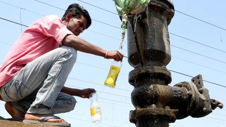 Un hombre indio recoge agua de una tubería.