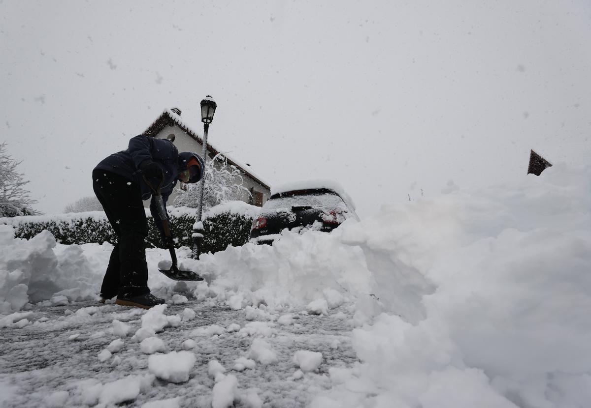 Una persona intenta limpiar de nieve para poder sacar su vehículo de una calle de la localidad de Espinal, en Navarra, donde una intensa nevada caída durante la jornada de este lunes cubre completamente la carretera.