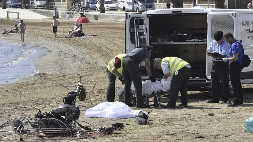 Los sanitarios introducen el cuerpo del varón en el vehículo mientras el parapente permanece destrozado en la arena.