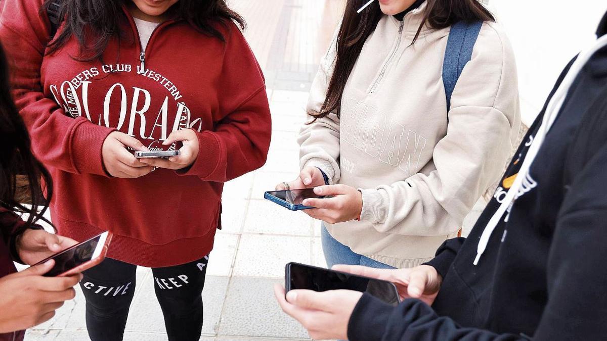 Jóvenes usan el móvil a la salida del instituto.