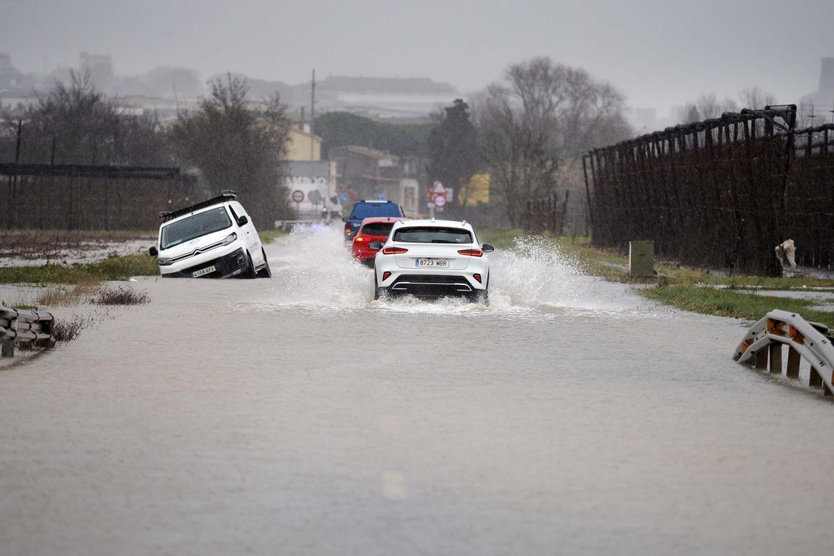 Vehicles circulen amb dificultats per una carretera inundada a Ullà, aquest dimarts, a causa de les fortes pluges del temporal Harry.