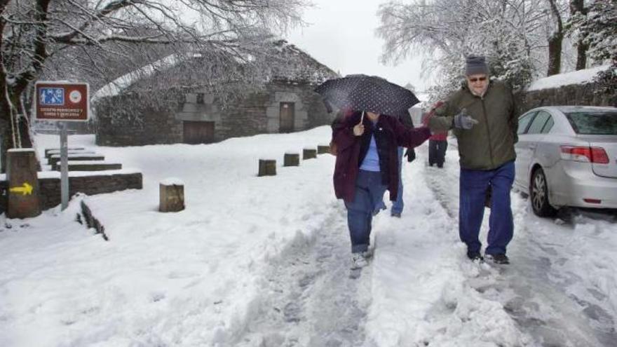 Dos turistas intentan mantener el equilibrio sobre la calzada nevada, ayer en O Cebreiro. / eliseo trigo