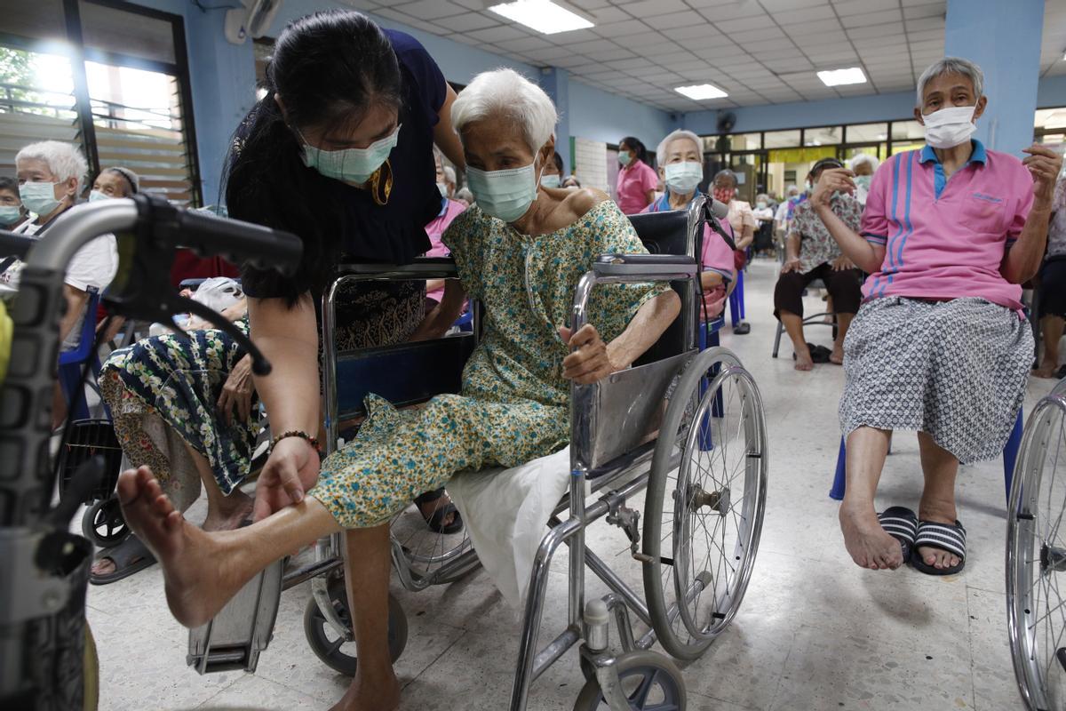 Una asistente ayuda a una anciana en silla de ruedas a levantar una pierna, durante los ejercicios matinales que realiza en la residencia Ban Bang Khae II en Bangkok.