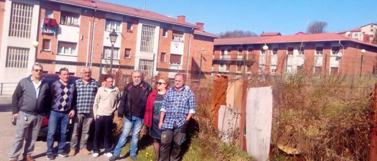 Por la izquierda, Víctor Fernández, Carlos Muñoz, José María Suárez, José Luis Gómez, Nel Ánxel Palacio, Manoli Casielles y Miroslav Lajer, junto a la parcela, a la derecha, donde se construirá uno de los bloques, con las viviendas afectadas por las grietas al fondo.