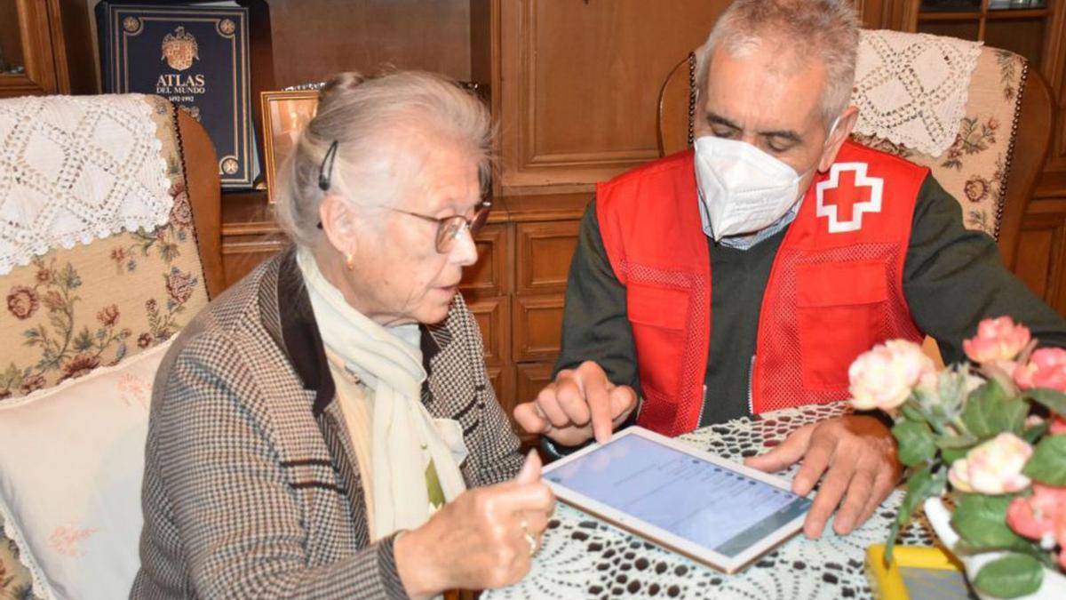 Un voluntario de Cruz Roja enseña a una persona mayor en su casa.
