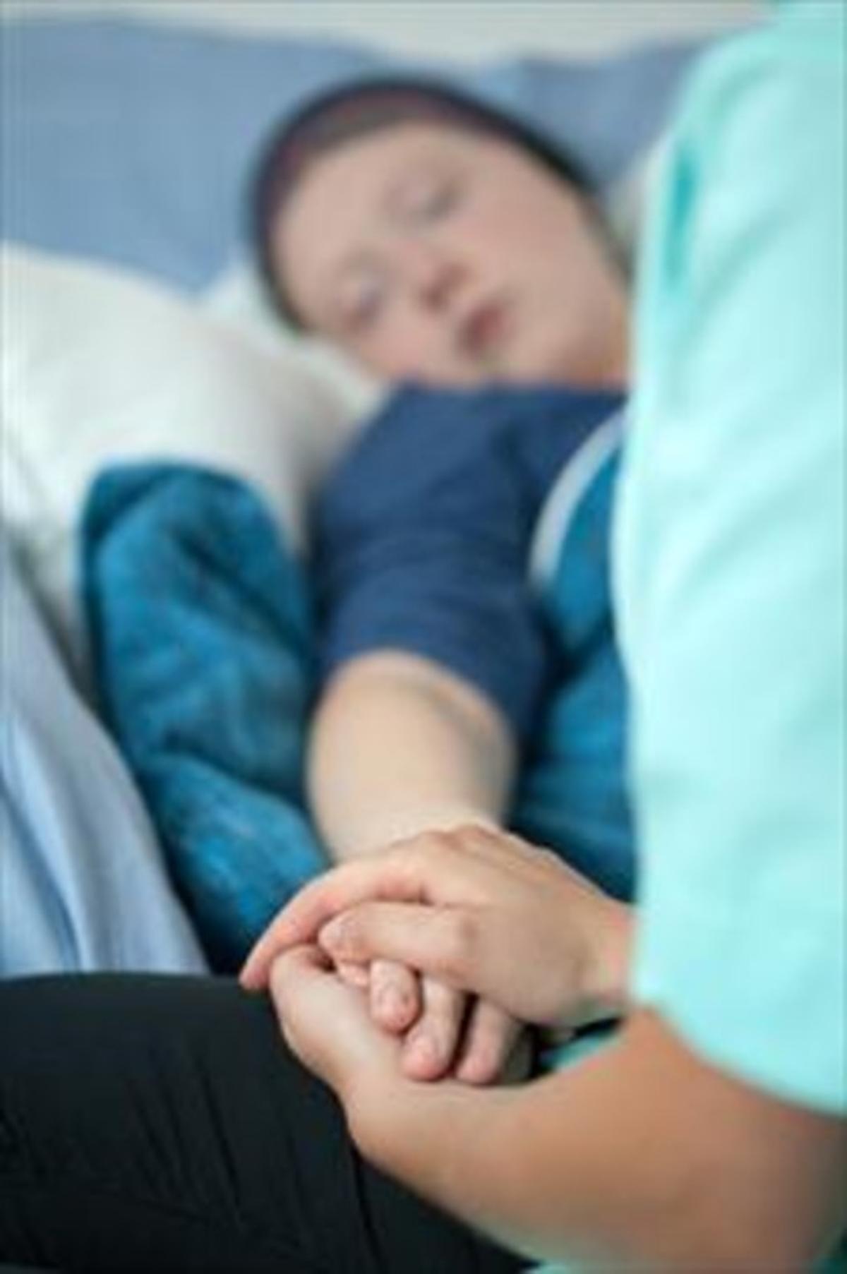 Una enfermera sostiene la mano de una enferma que recibe curas paliativas.
