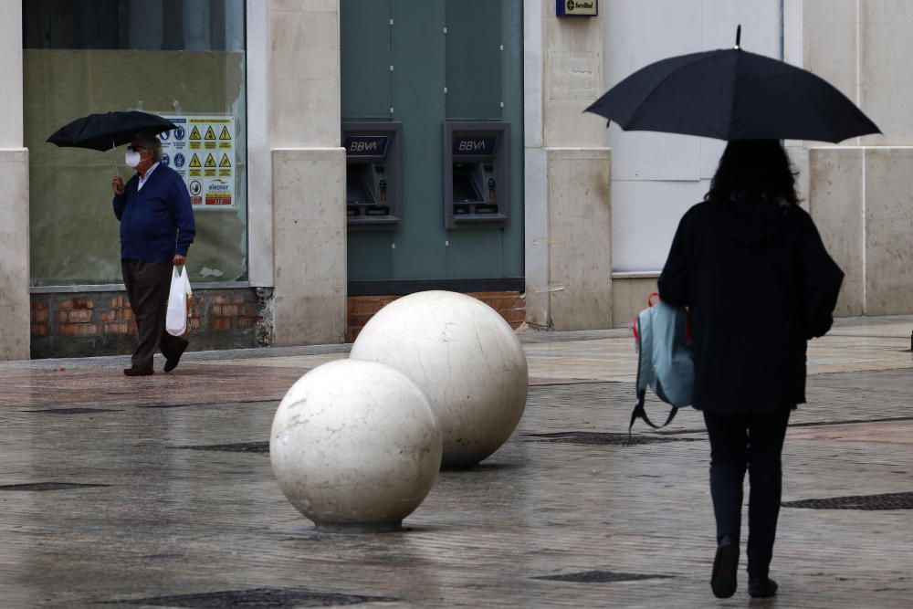 Imágenes de una lluviosa mañana de jueves en el centro de Málaga, donde al paisaje ya habitual de pocas personas y la mayoría de ellas con guantes y mascarillas se le han añadido los preparativos de bares, cafeterías y terrazas que se preparan para el inminente cambio de fase de la desescalada de la ciudad.