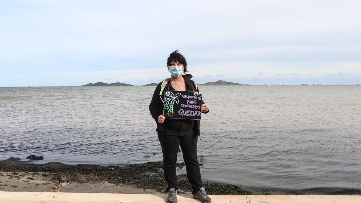 Una mujer sostiene una pequeña pancarta a la orilla del mar.