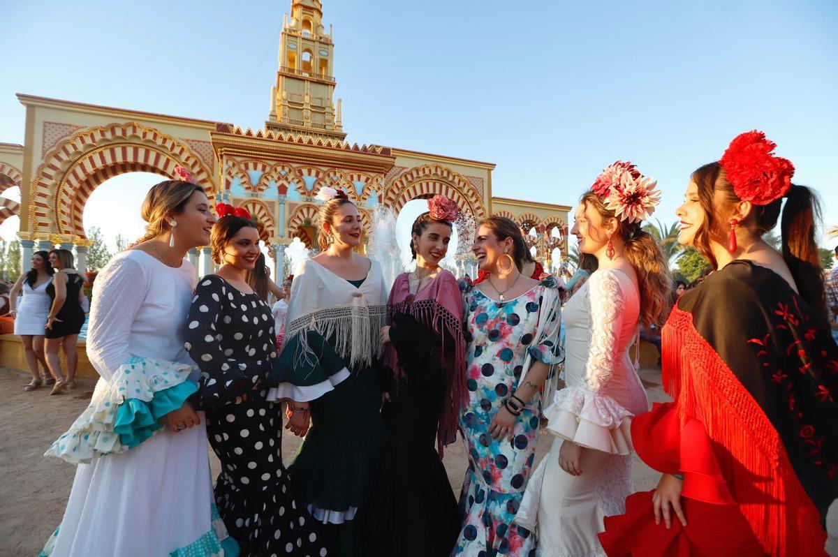 Varias mujeres posan vestidas con trajes de gitana ante la portada de la Feria de Córdoba.