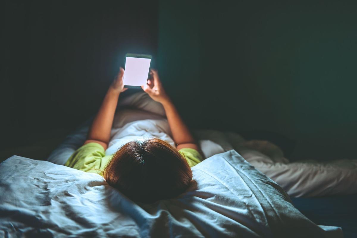 Un niño mirando el móvil en su cama.