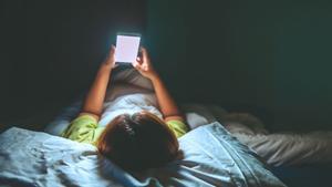 Un niño mirando el móvil en su cama. 