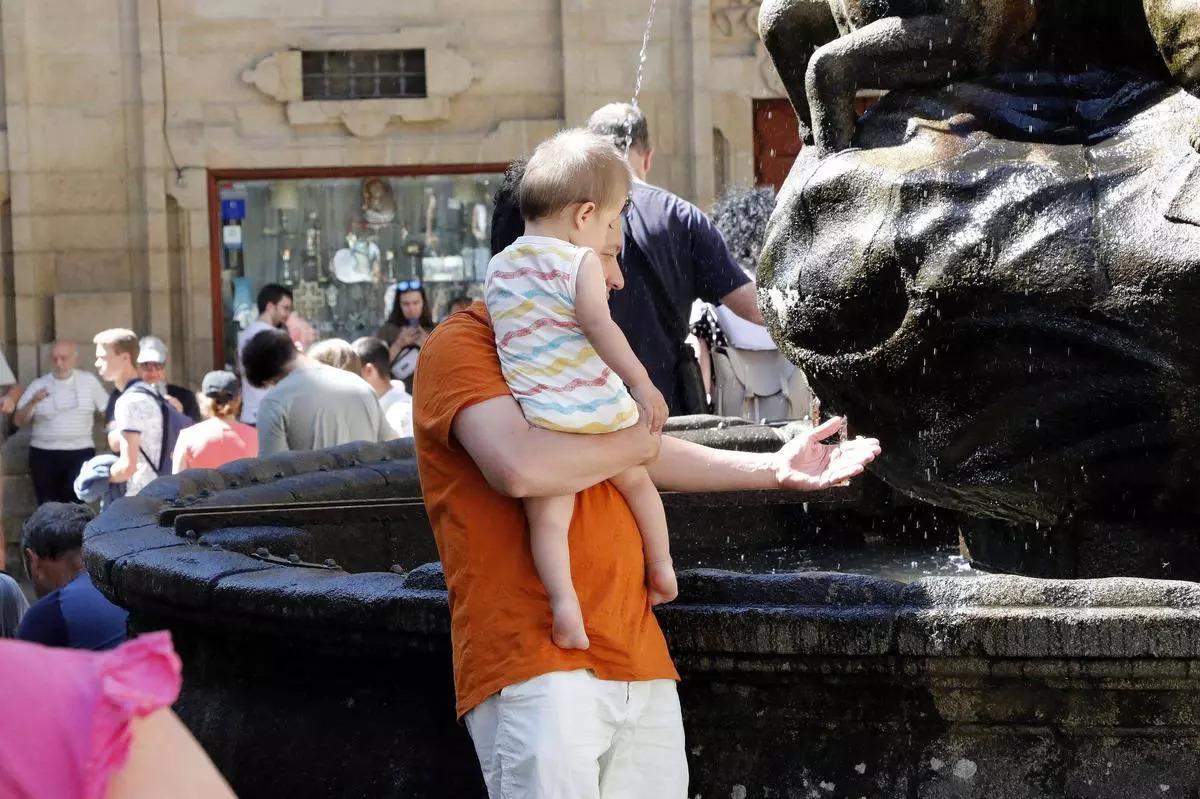 Un padre refresca a su hijo con el agua de la fuentes de los Caballos de la praza das Praterías en Santiago