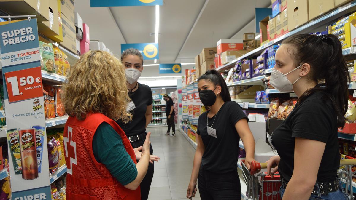 Una voluntaria de Cruz Roja habla con varias jóvenes empleadas en un supermercado.