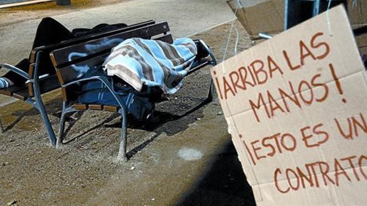 Unos indignados duermen en un banco de las inmediaciones del parque de la Ciutadella junto a una pancarta de protesta, el pasado miércoles.