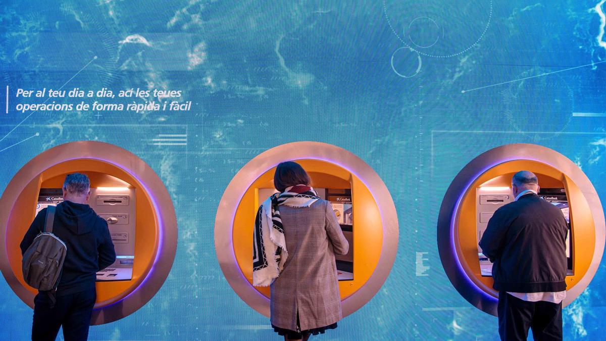 Clientes operan en un cajero automático en un banco en València
