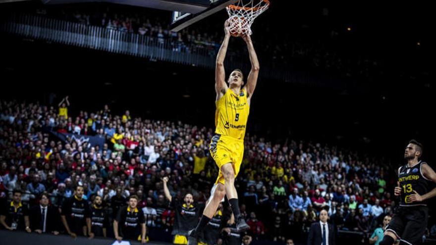 Nico Brussino -Iberostar Tenerife-, a punto de colgarse del aro del Antwerp, con el banquillo canarista a su espalda.