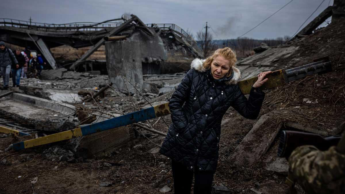 Una mujer hace un alto en el camino tras cruzar un puente destruido en su huida de la ciudad de Irpin, en Ucrania.