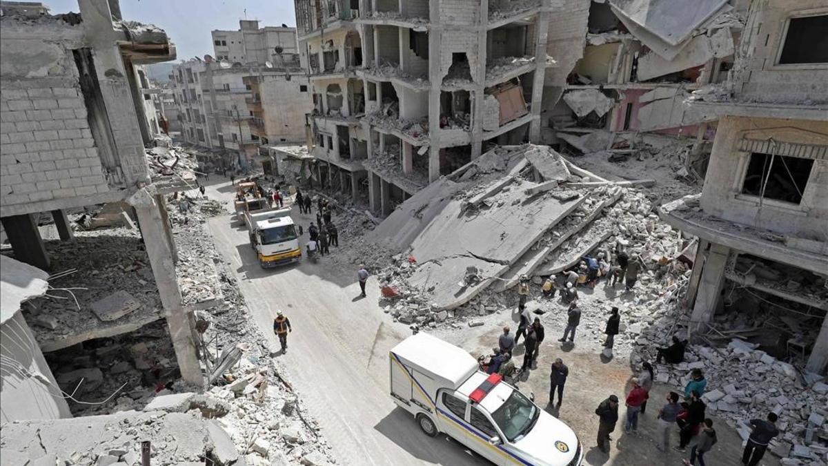 La gente observa a miembros de la Defensa Civil siria buscar entre los escombros de un edificio derrumbado tras una explosión en la ciudad de Jisr al Shughur, en el oeste de la provincia siria de Idlib, bajo control de Hayat Tahrir al Sham.