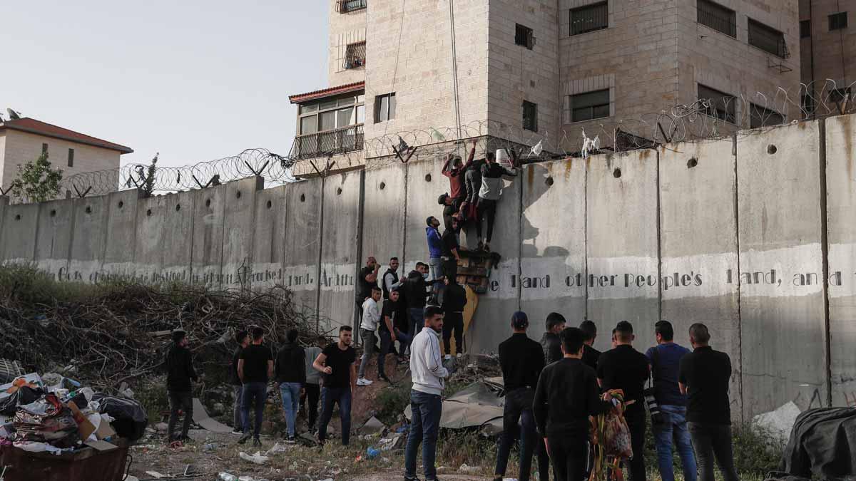 Palestinos intentando saltar el muro que separa el pueblo de  A-Ram de Jerusalén para acceder a la Explanada de las Mezquitas en el último viernes de Ramadán.