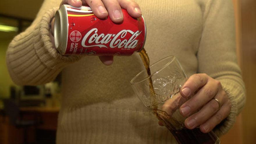 Una persona deposita el contenido de una lata de Coca Cola en un vaso con el distintivo de la marca de bebidas