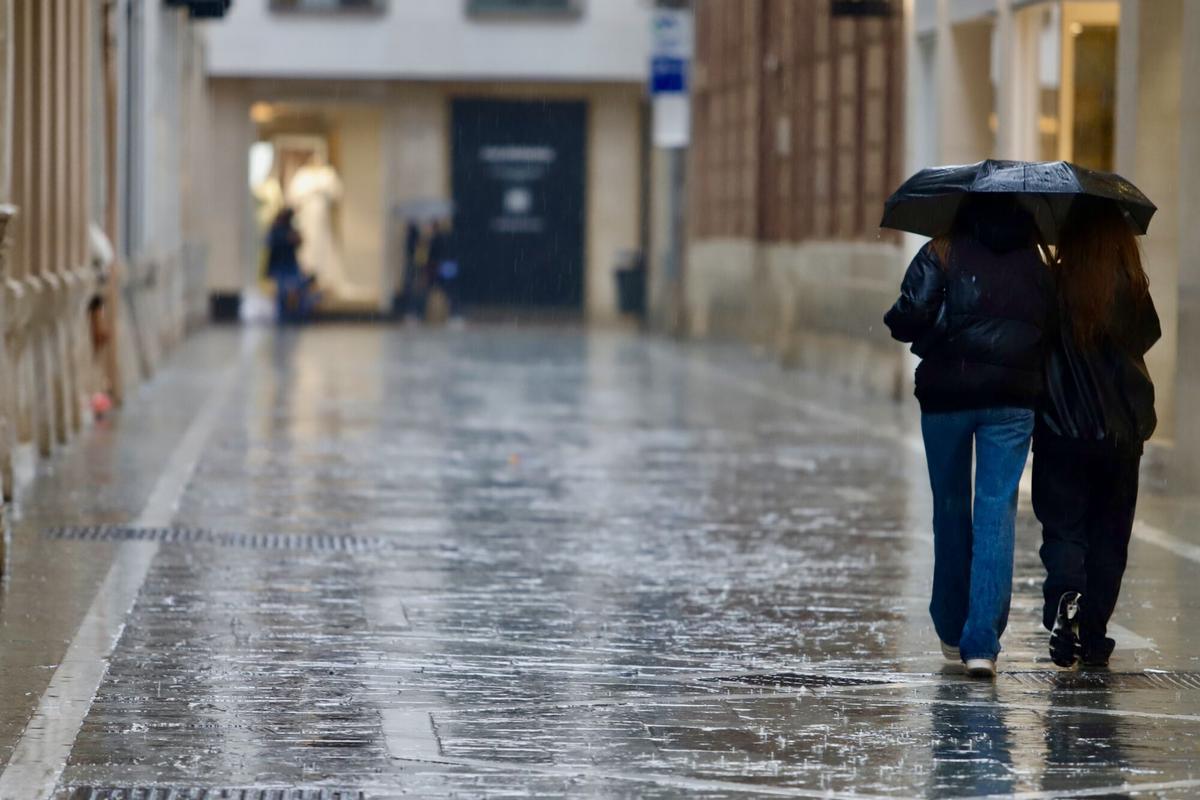 Dos personas pasean con paraguas por las calles de la capital