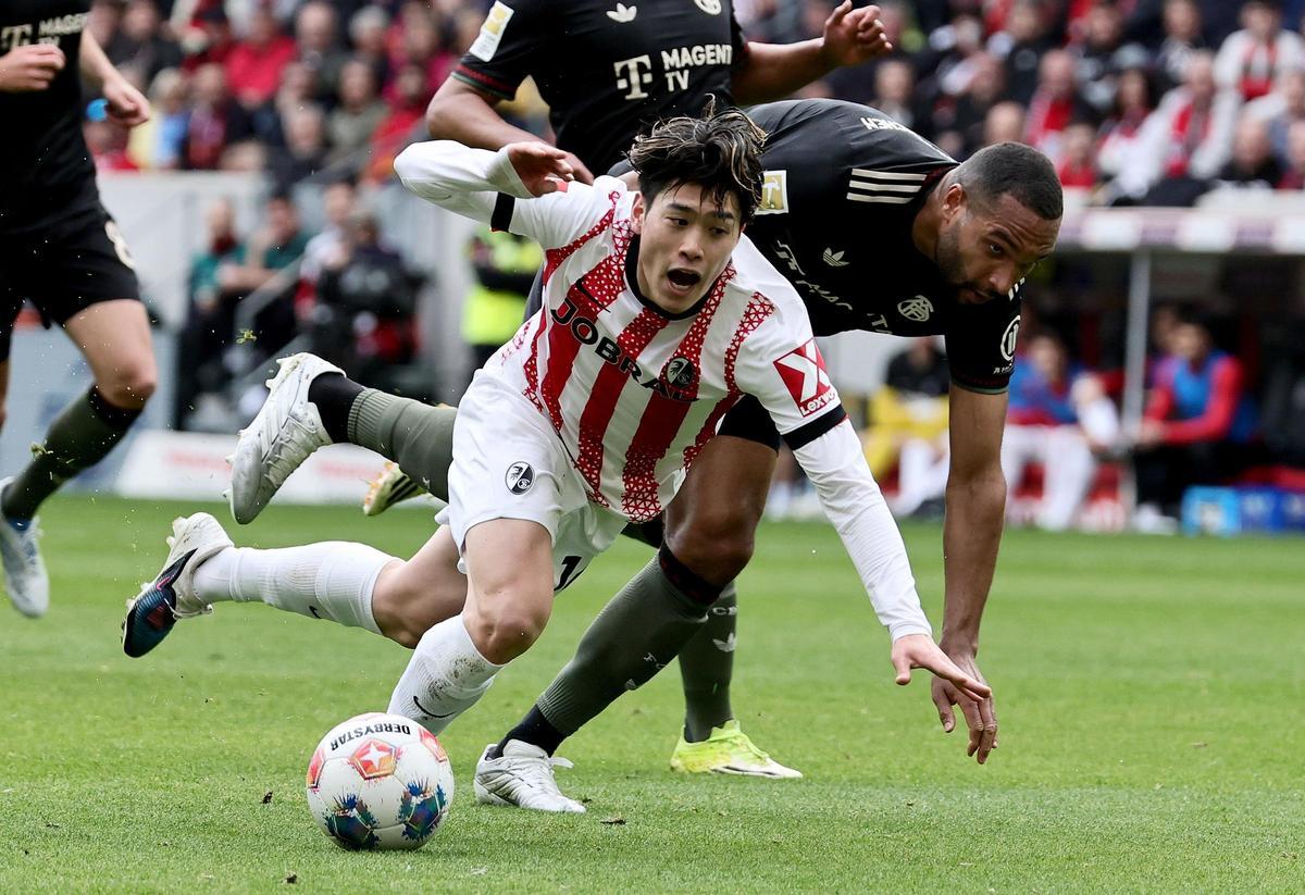 Yuito Suzuki, del Friburgo, cae ante Jonathan Tah en el último partido de la Bundesliga contra el Bayern.