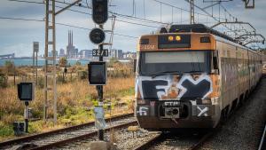 Un tren lleno de grafitis transita por la R1 de Rodalies, con las Tres Xemeneies de Sant Adrià al fondo