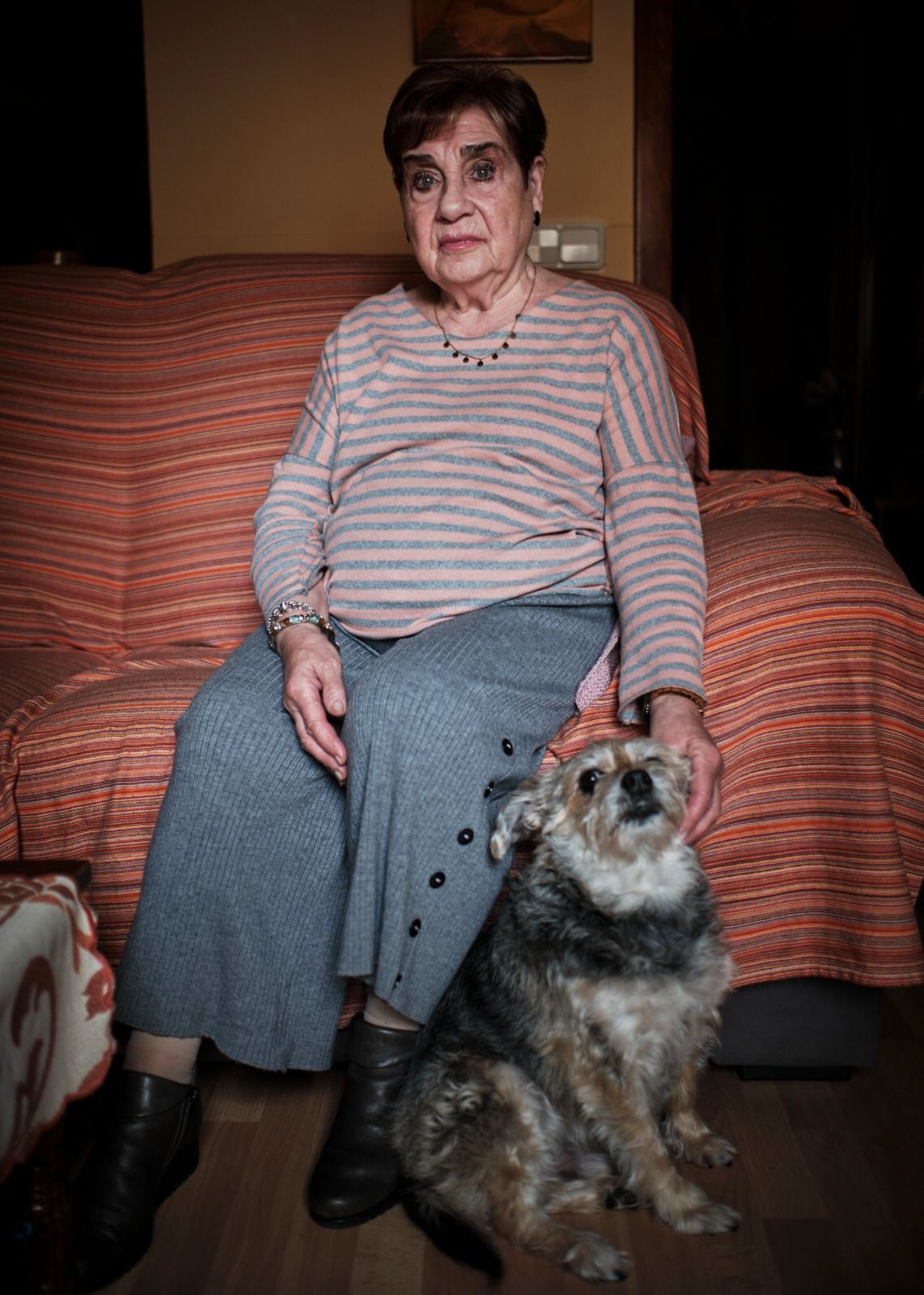 Paquita con su perro sentada en el sofá de su vivienda.