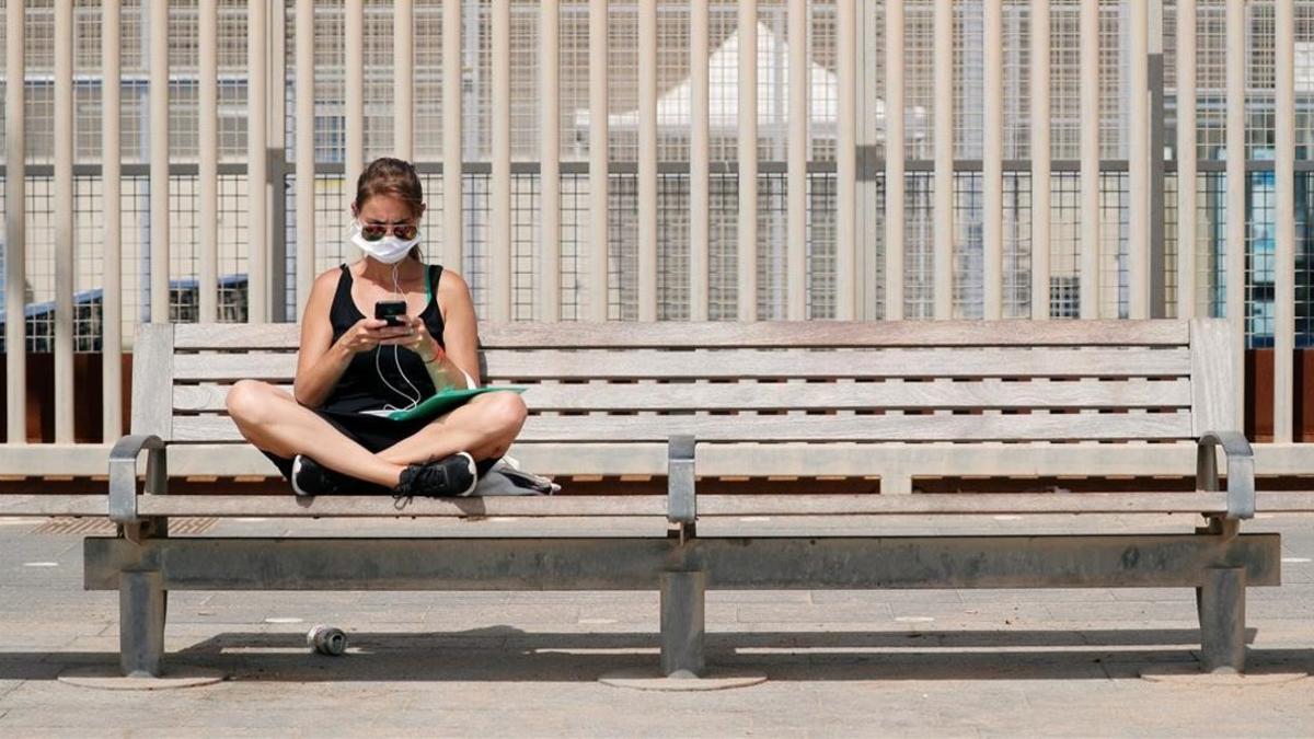 Una mujer con mascarilla, en un banco de Barcelona