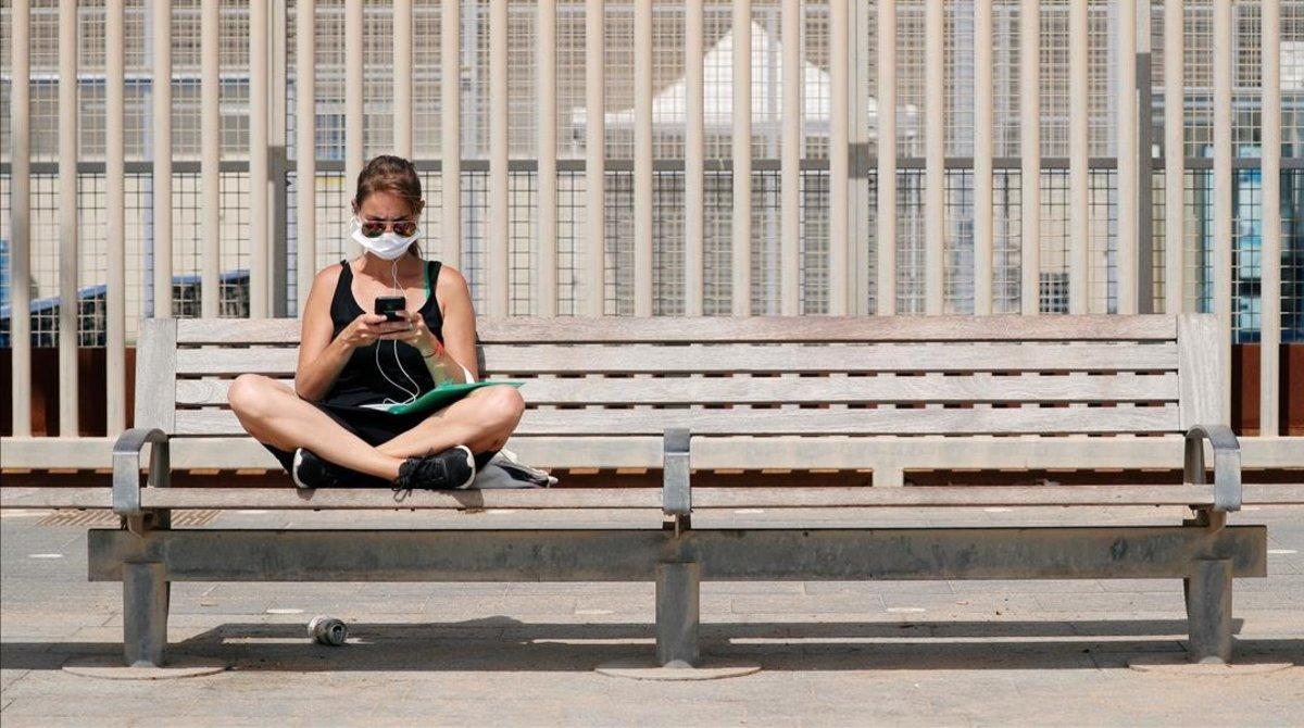 Una mujer, con mascarilla por el coronavirus, en un banco de Barcelona.