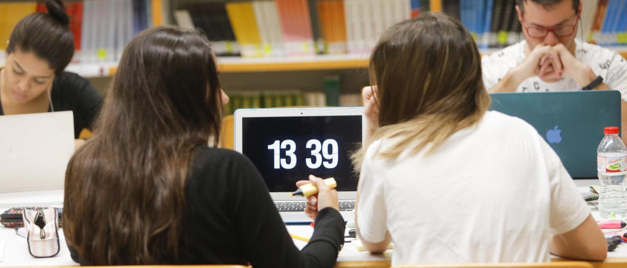 Dos jóvenes conversan mientras estudian en una biblioteca de la UV.