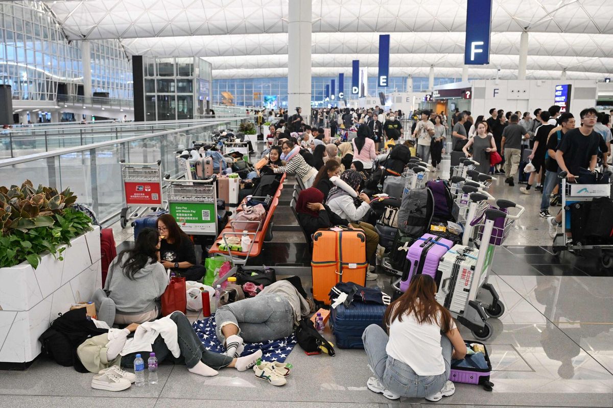 Outbound passengers sit and wait while others queue to check-in as flights resume at the Hong Kong international airport, while Typhoon Wipha moves away from the city on July 20, 2025. A representative from Hong Kongs Airport Authority earlier said that around 500 flights have been cancelled due to the weather, while around 400 flights were scheduled to take off or land later in the day. (Photo by Peter PARKS / AFP)