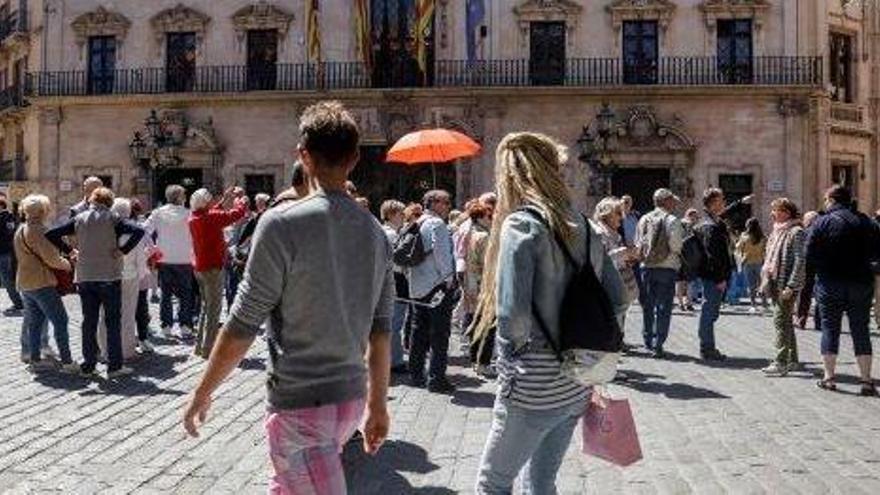 Un guía, sujetando un paraguas naranja, con un grupo de turistas en la plaza de Cort de Palma.