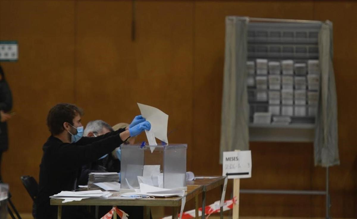 El miembro de una de las mesas introduce en la urna uno de los votos llegados por correo en el pabellón de la España Industrial aprovechando un momento sin votantes.