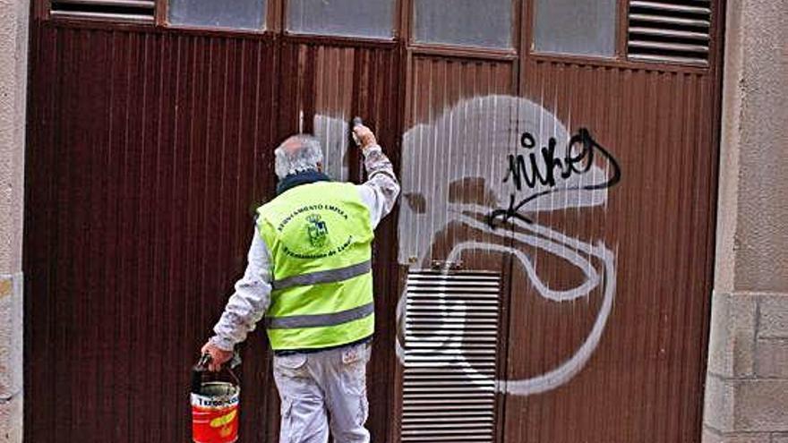 Un trabajador del plan de empleo tapa pintadas en un garaje.