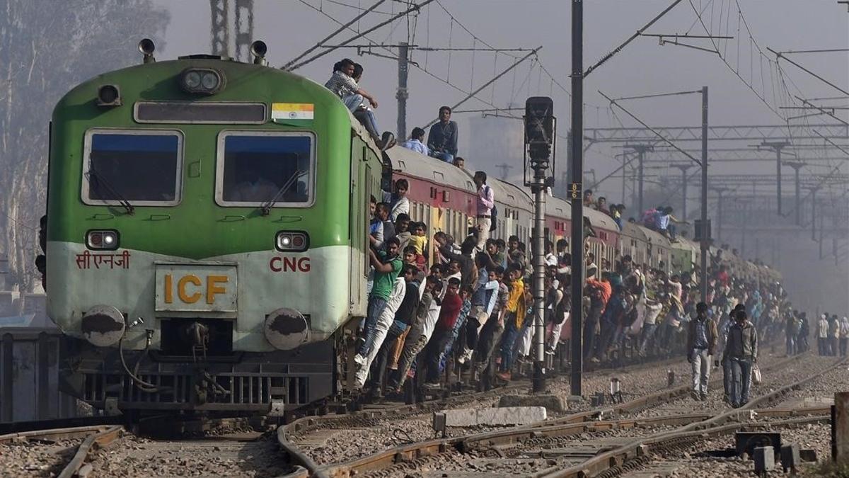 Pasajeros indios se aferran a un tren en una estación de las afueras de Nueva Delhi, India. 