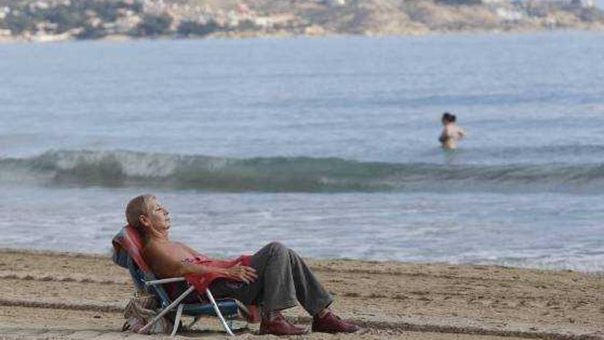 Una persona toma el sol ayer en la playa del Postiguet. Al findo una mujer bañándose