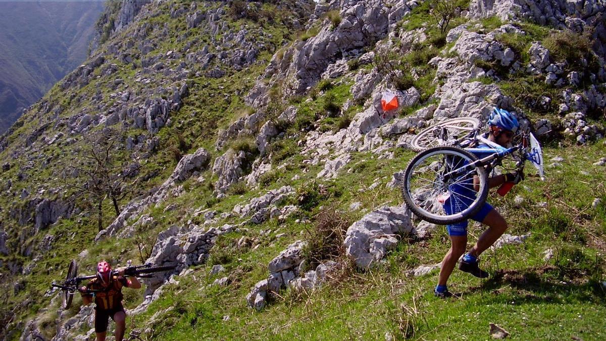 Dos 'raiders' escalan una montaña con sus bicicletas a cuestas durante una prueba de orientación.