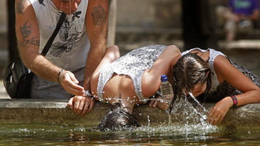 Varios turistas se refrescan en una fuente.