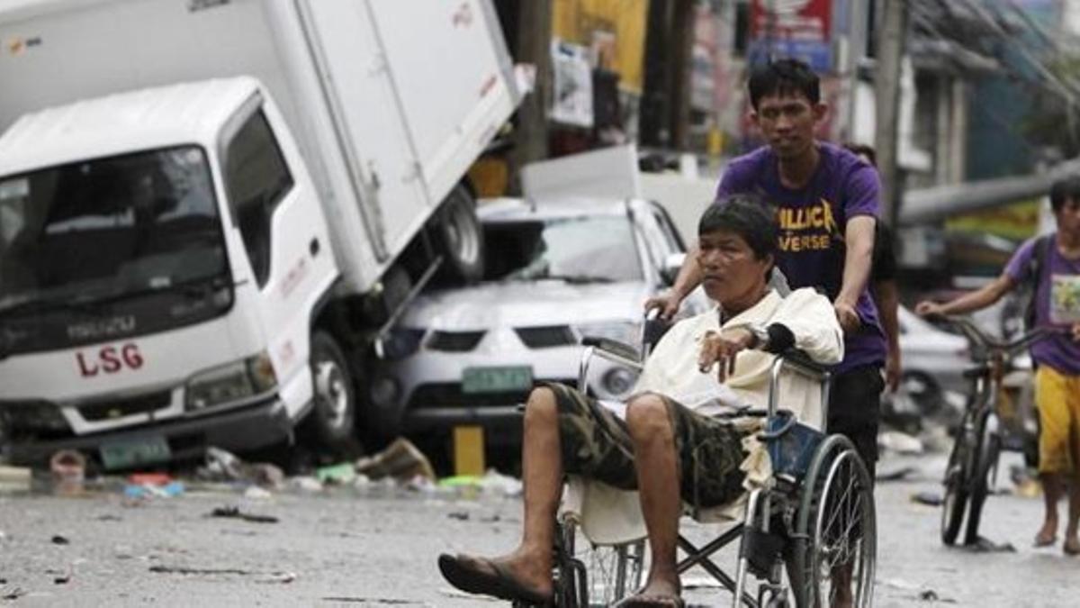 Varias personas recorren una calle de Tacloban, donde decenas de miles de supervivientes sufren la carencia de alimentos y agua.