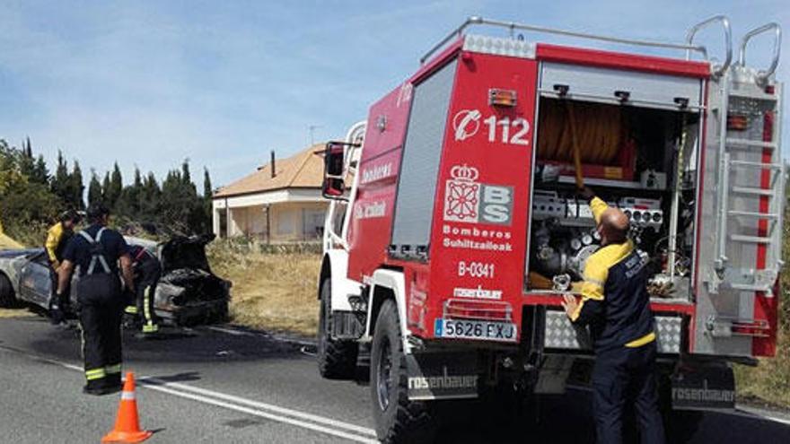 Los bomberos con el coche incendiado.